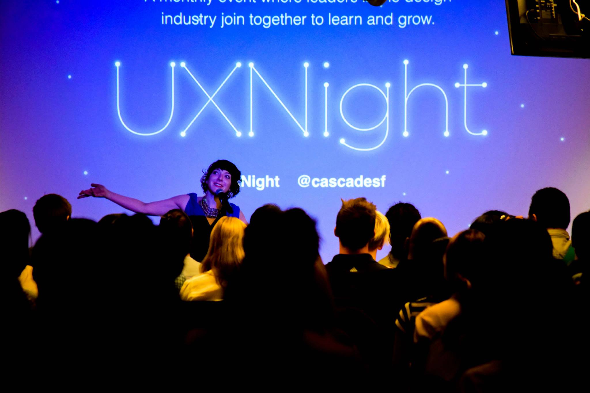 An audience silhouetted against a large projected UXNight title slide